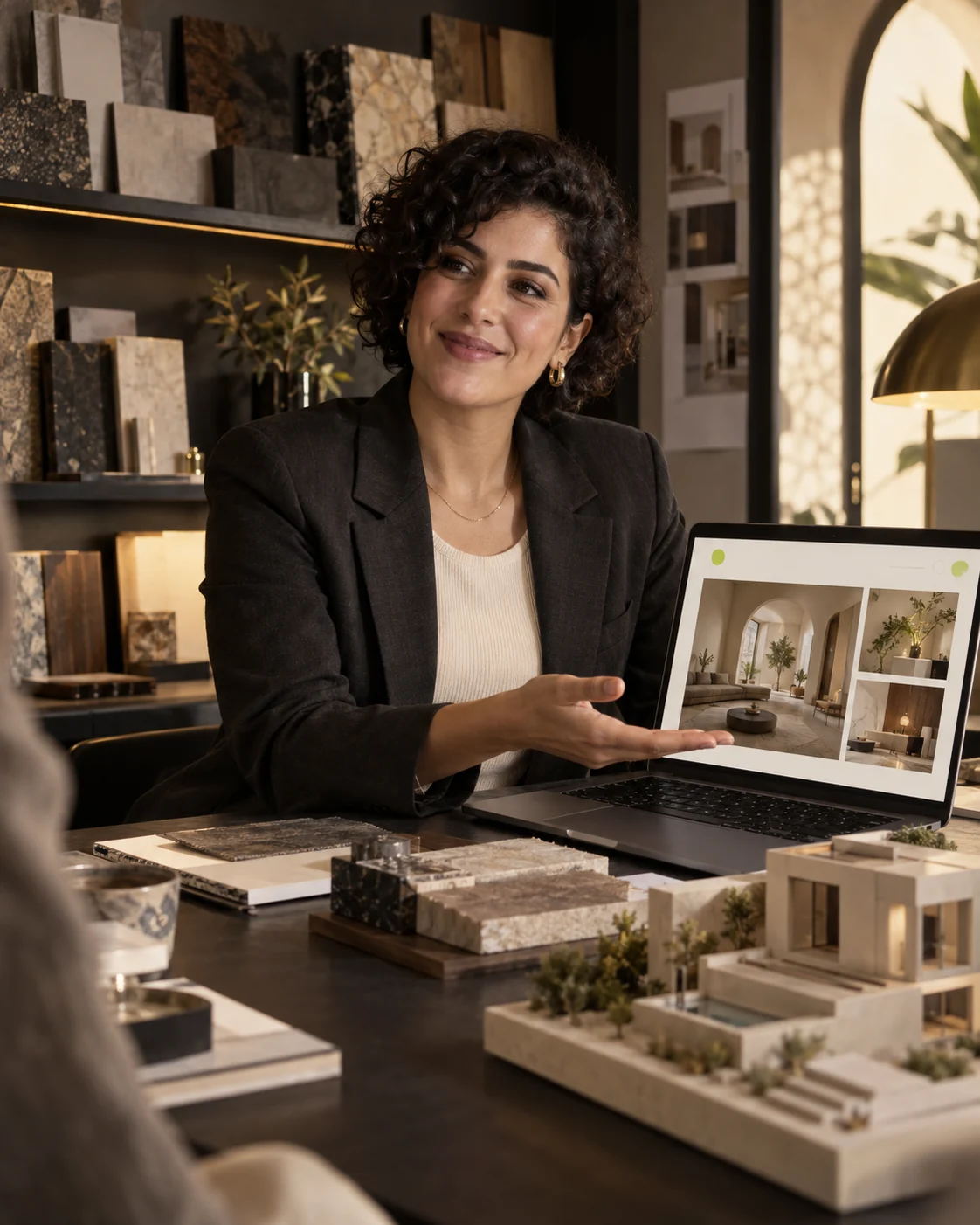 A smiling architect presenting her portfolio website beside material samples and an architectural model.