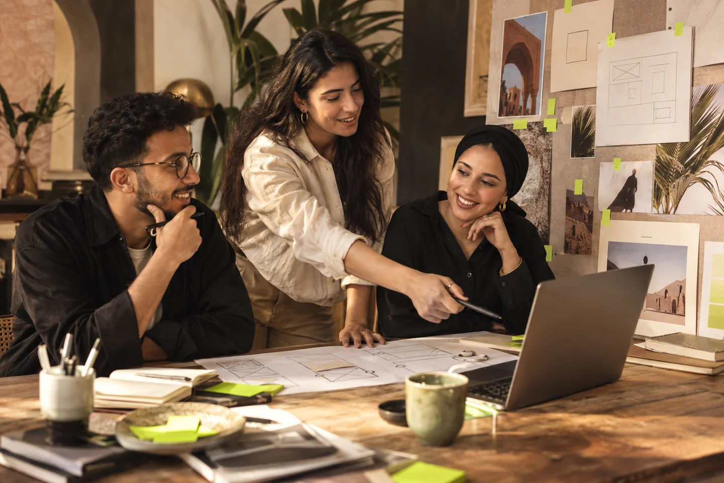 A creative team develops a project around a wall of sketches, layouts and a laptop.