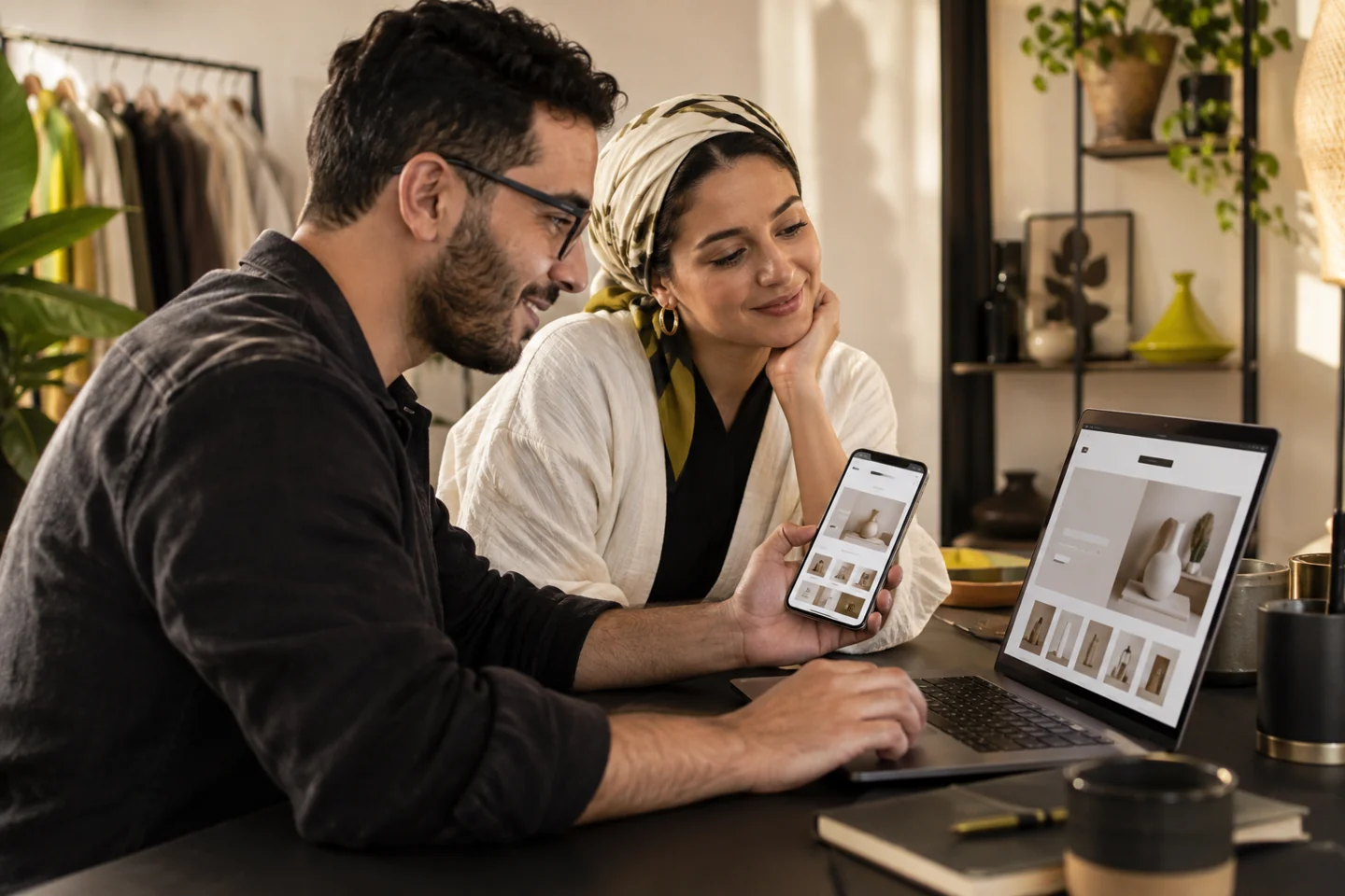 A developer and business owner check an online store together on a phone and laptop.